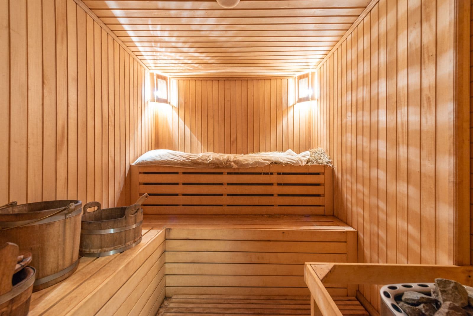 Interior de una sauna de madera con bancas, cubetas y estufa de piedras